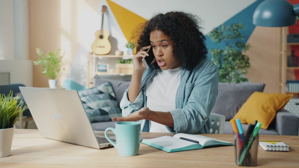 Young woman talking on phone at laptop desk